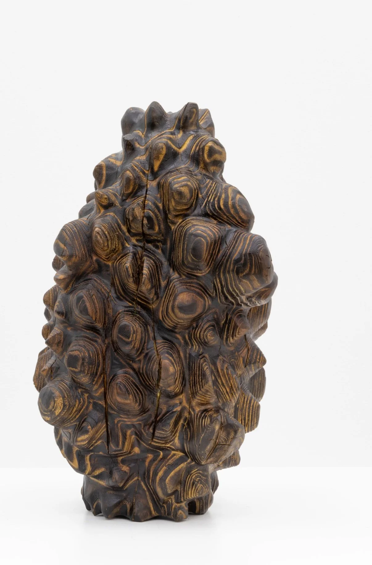 Born of Wood — a dense cluster of carved wooden whorls forming a standing organic mass, on white