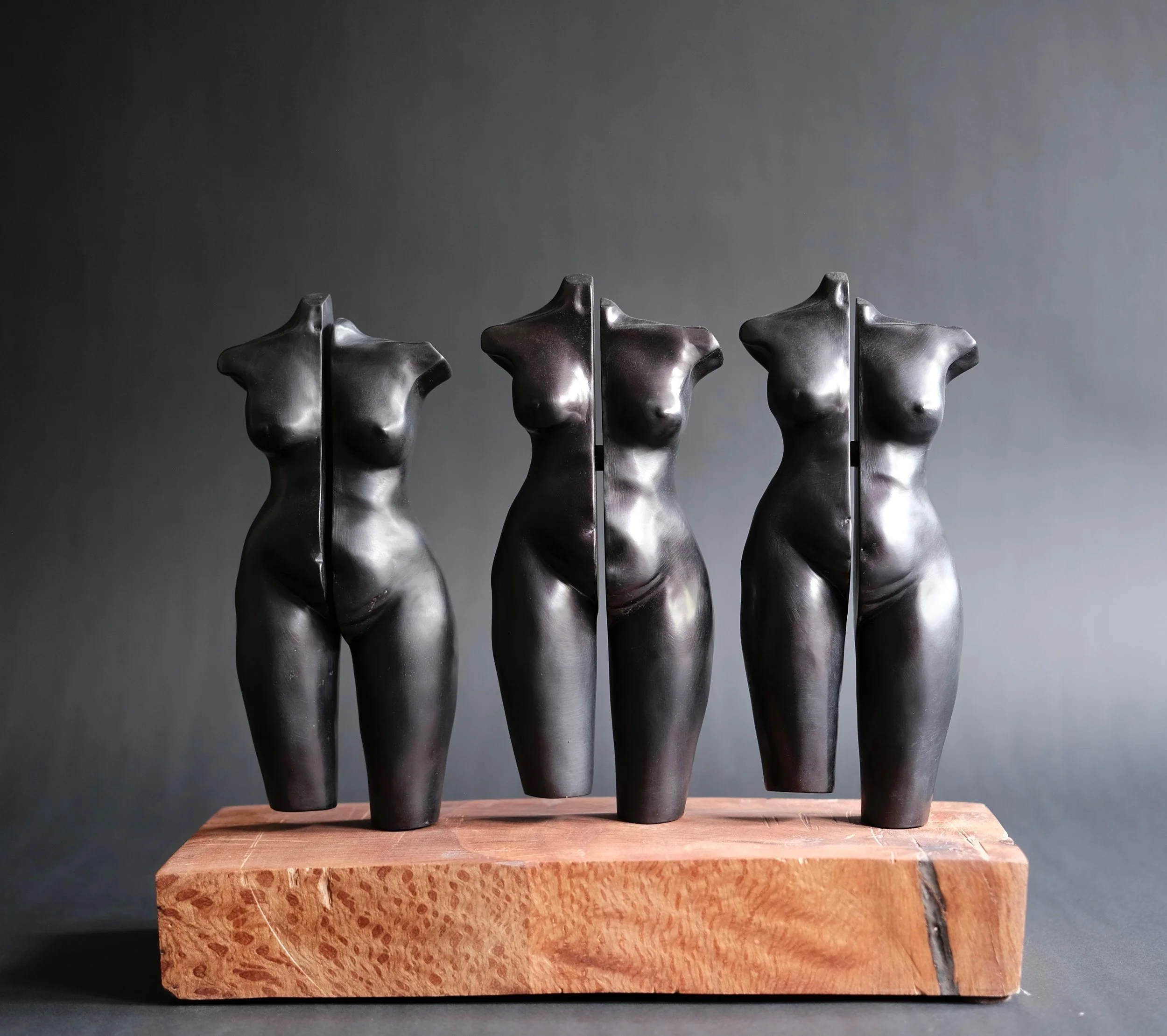 Distancing — three black ceramic torsos, each split vertically down the center, standing on a redwood base
