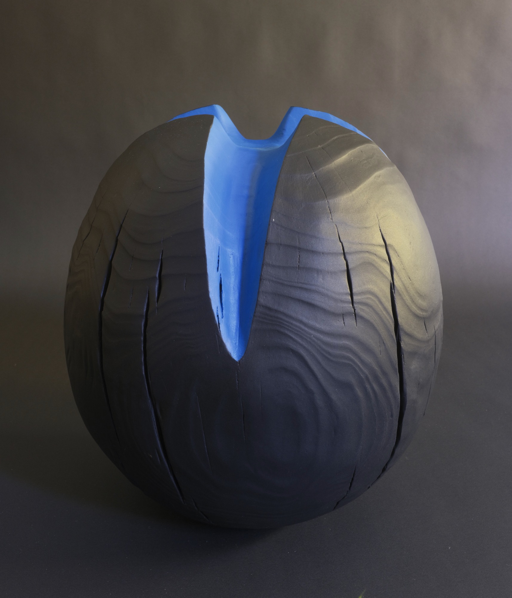 It was tiime to leave — charred black sphere with a carved electric-blue cleft, front view