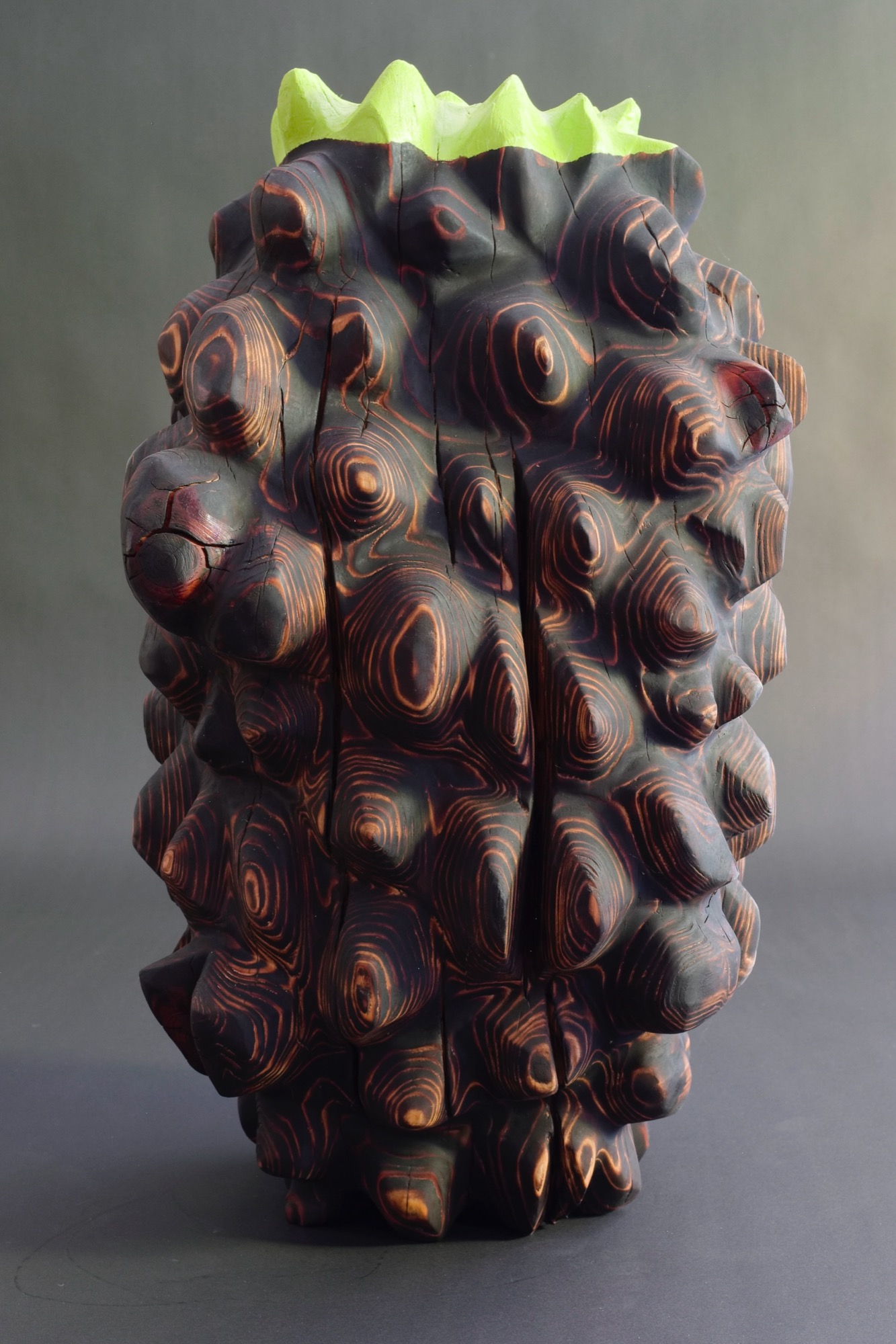 New growth — a densely carved, charred redwood vessel with knotted whorls and an acid-green carved rim